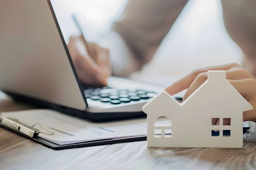 Person bearbeitet Akten, Modell eines Hauses im Vordergrund